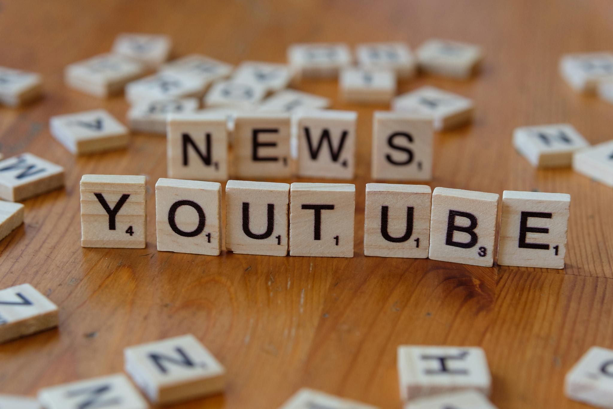 Scrabble tiles spelling words on wooden surface, focusing on YouTube and News.
